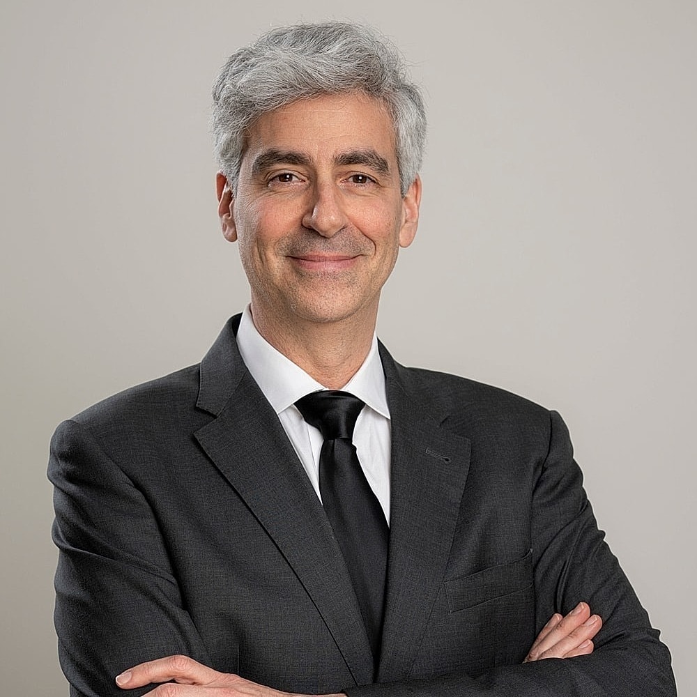 Smiling man in a suit, arms crossed confidently.