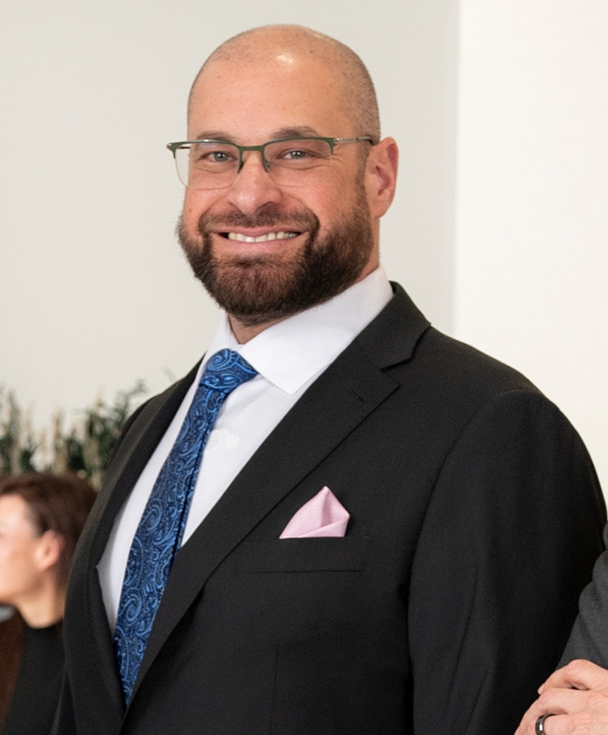 Man in suit with beard and glasses smiling.