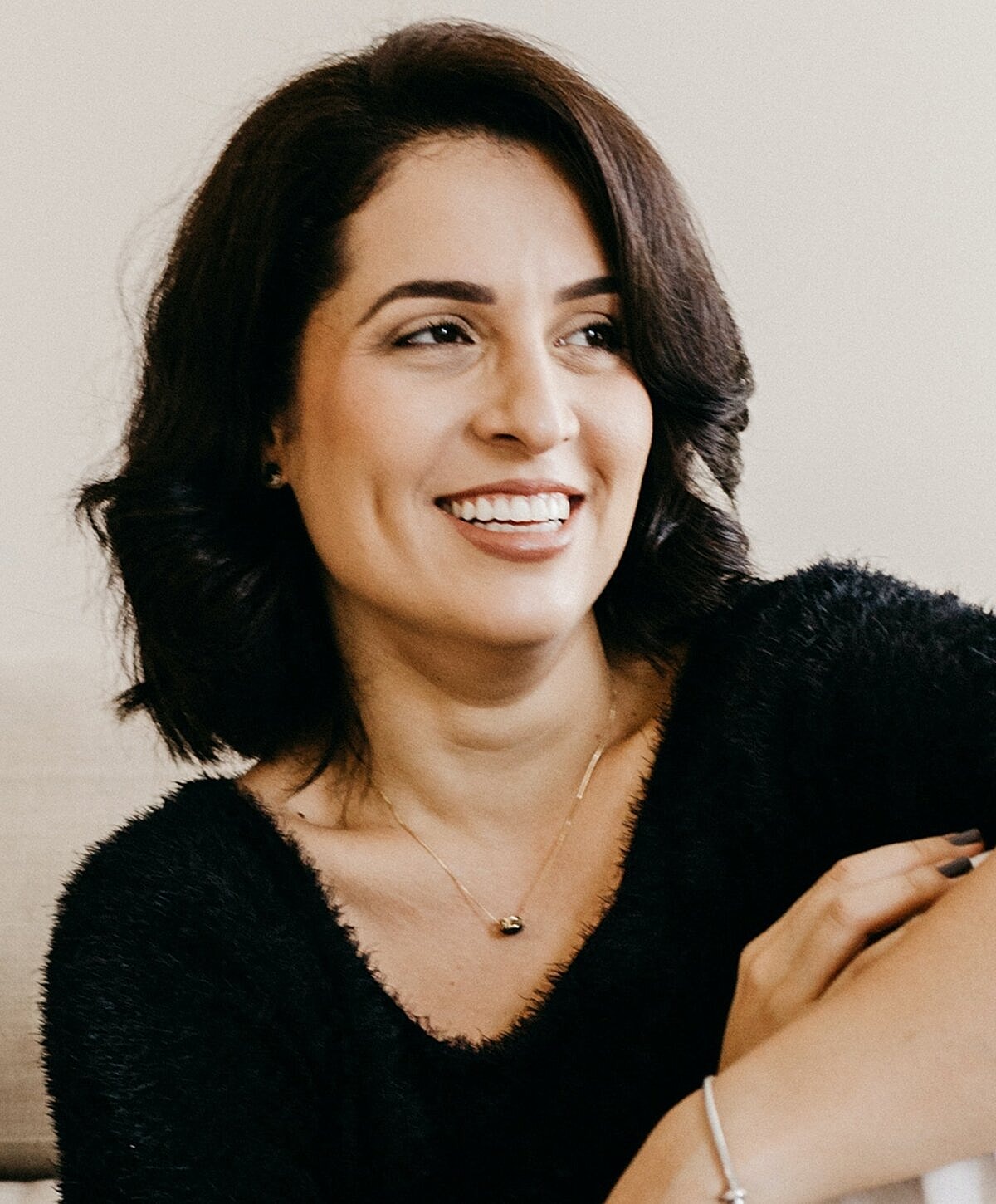Smiling woman wearing black sweater and jewelry.