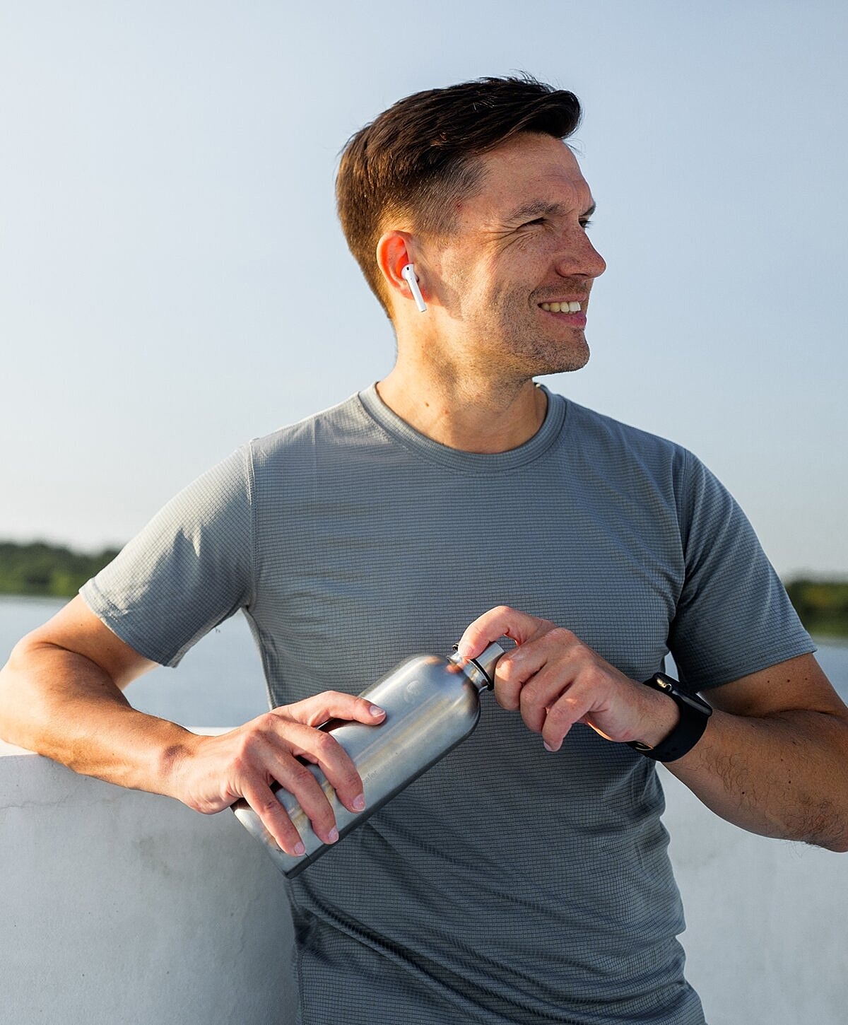 Man in activewear holding water bottle outdoors.