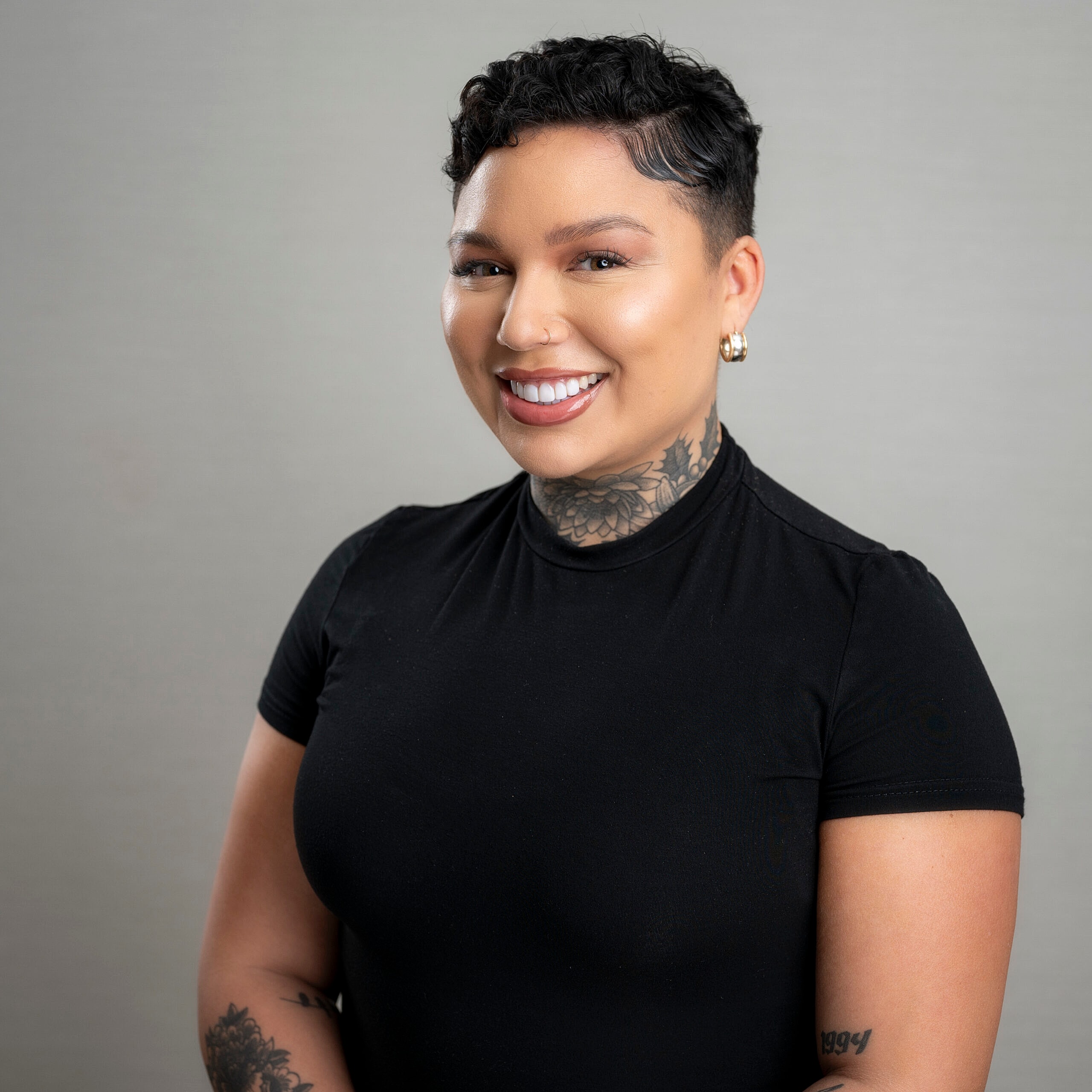 Smiling person with tattoos wearing a black shirt.