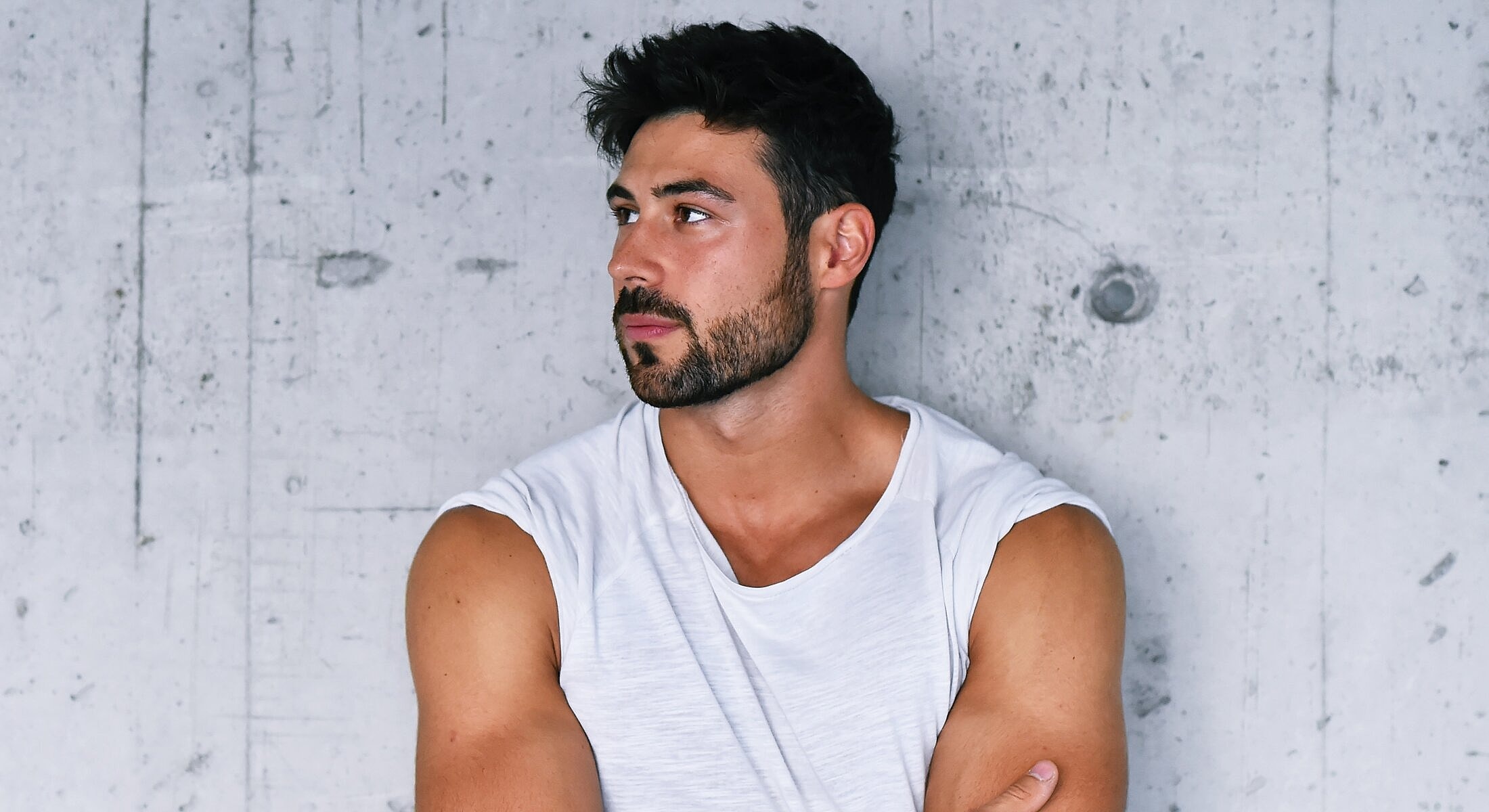Man in sleeveless shirt against a concrete wall.