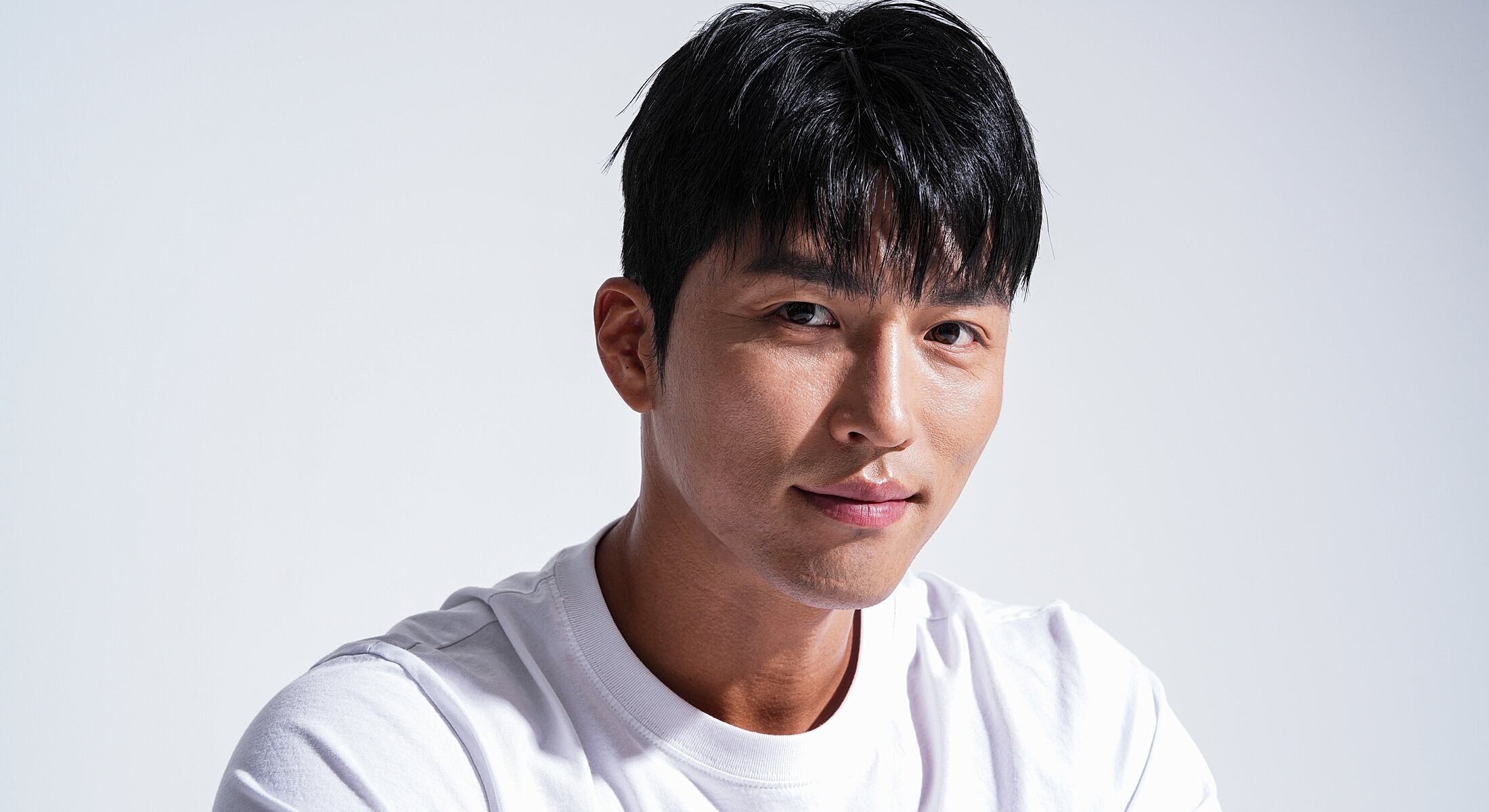 Man with short black hair, smiling in white shirt.