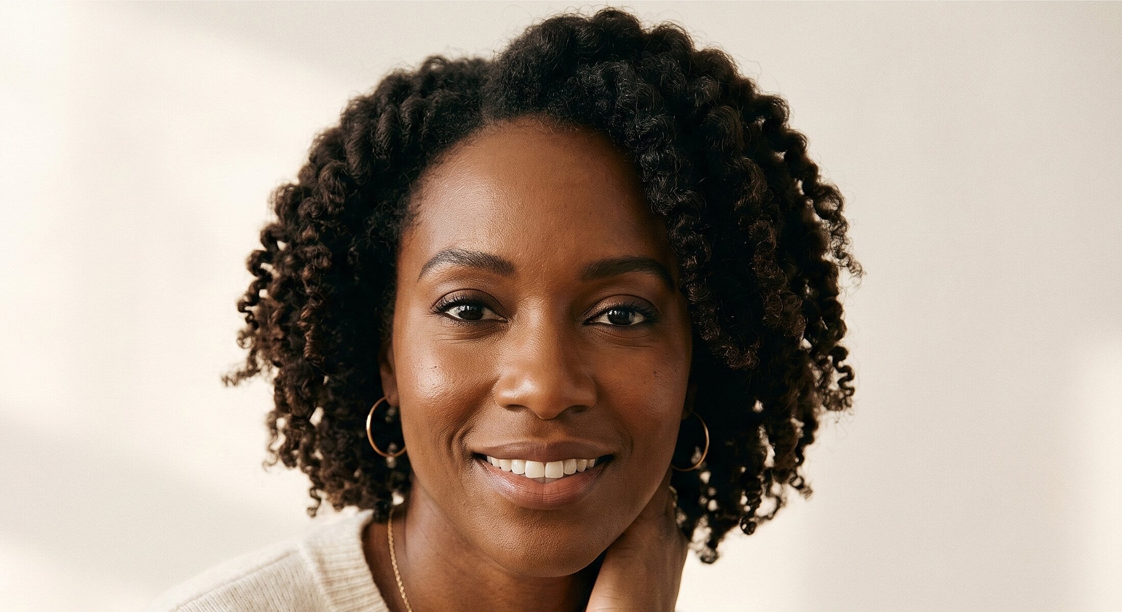 Smiling woman with curly hair and neutral background.