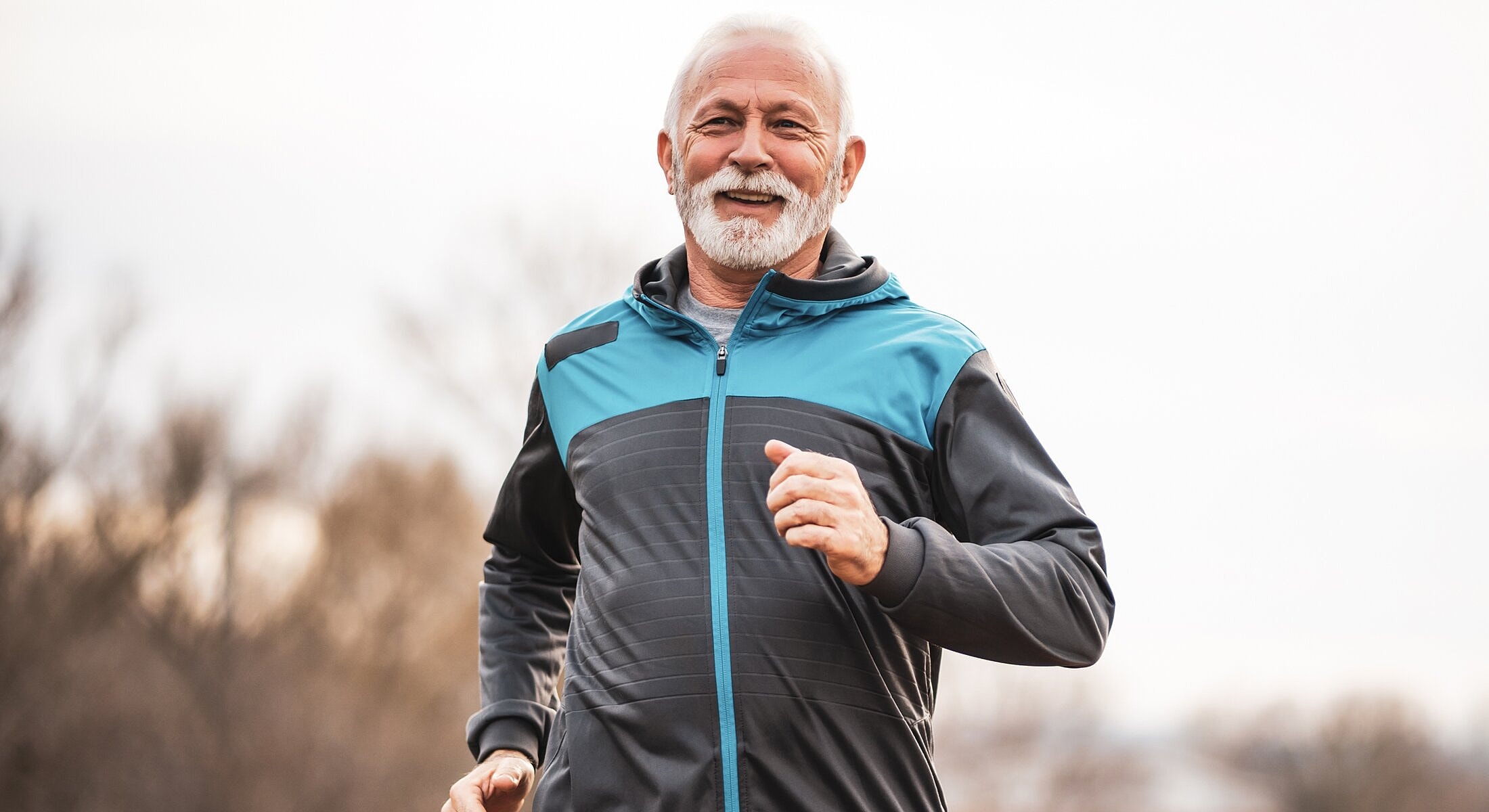 Elderly man jogging outdoors in athletic clothes.